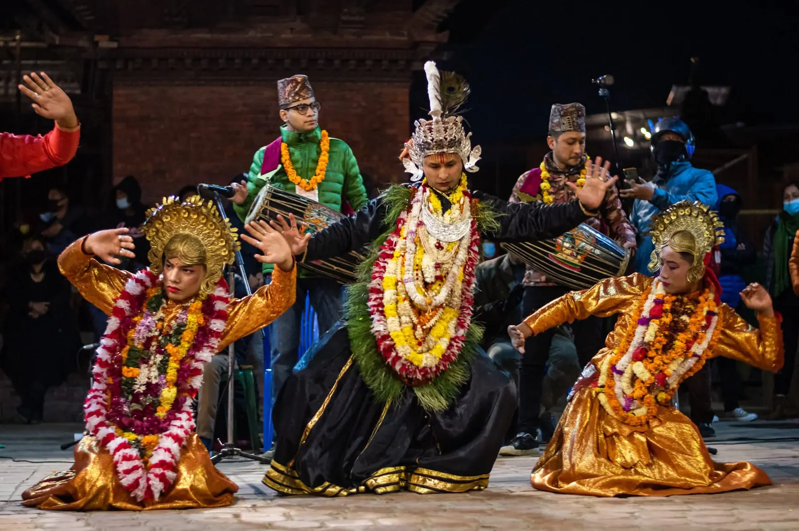 Crowned dancers in garlands kneel and pose together in front of the musicians