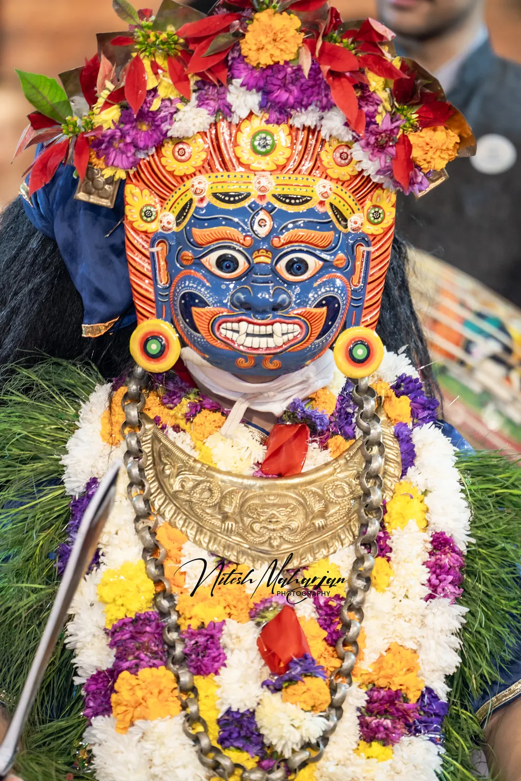 Close-up of a blue painted mask with a flower crown and garlands